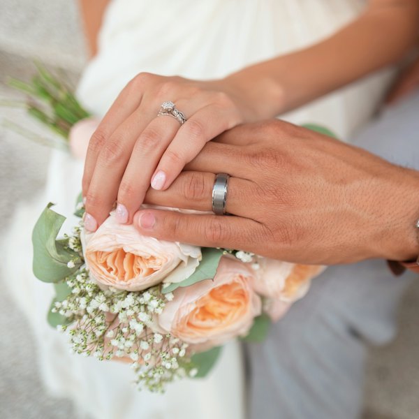 Couple's hands with rings holding a flower bouquet