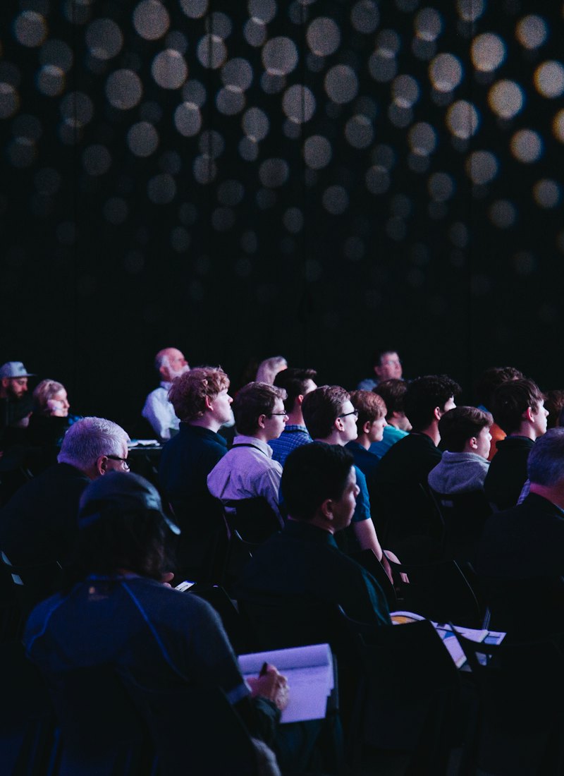 Audience seated in a darkened auditorium facing a stage