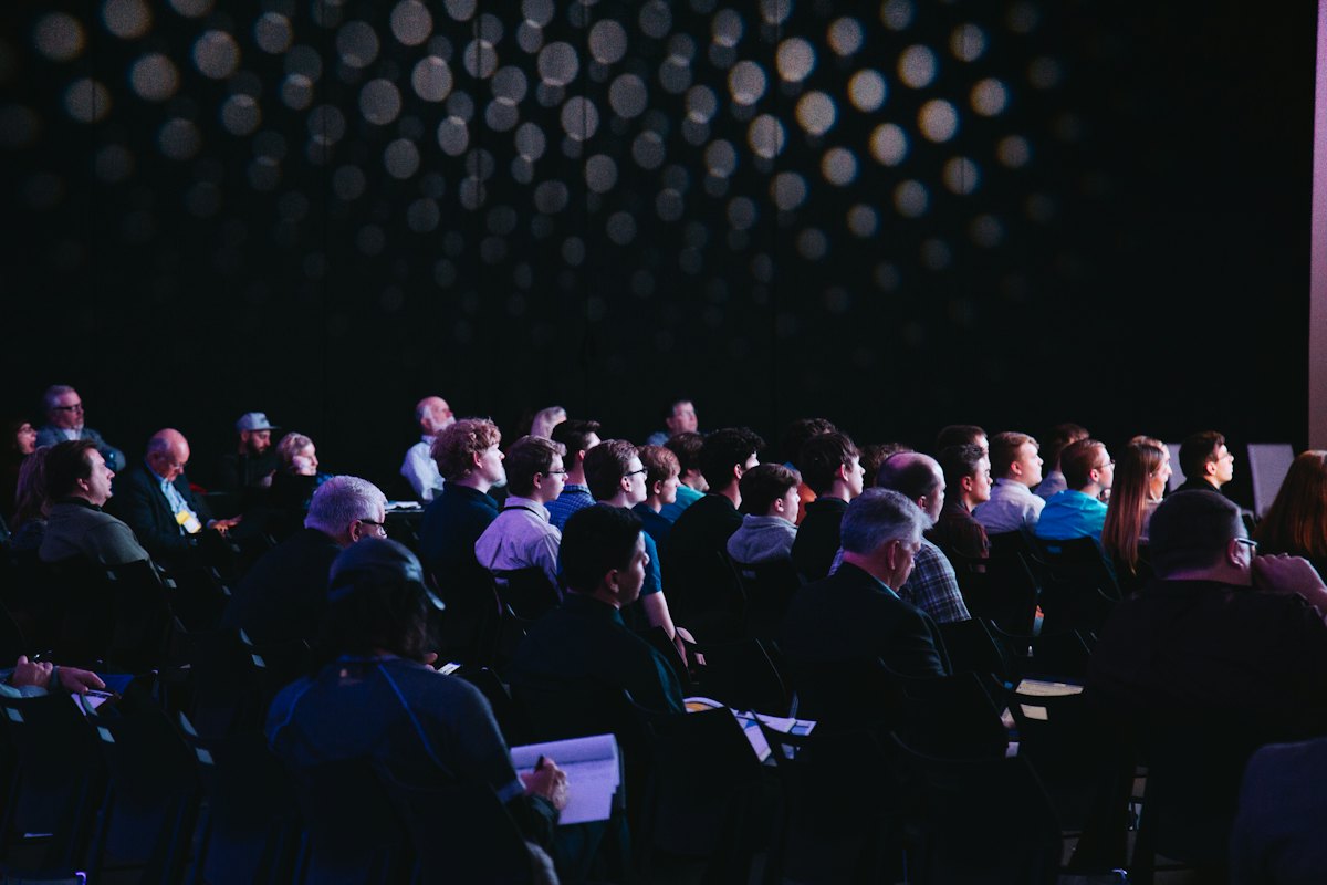 Audience seated in a darkened auditorium facing a stage