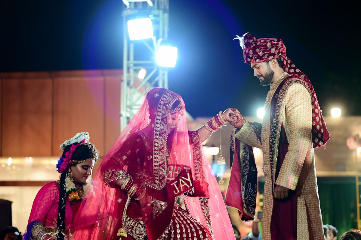 Bride and groom in traditional attire under a colourful fabric canopy at night
