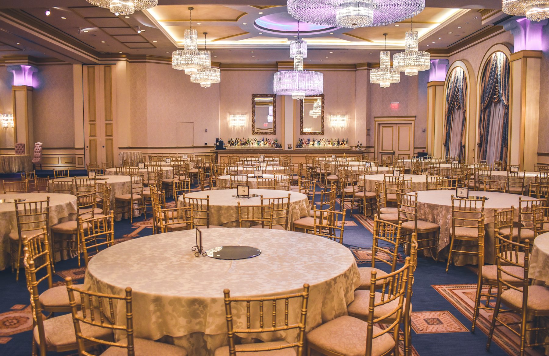 Grand ballroom with chandeliers and gold-draped round tables prepared for a gala